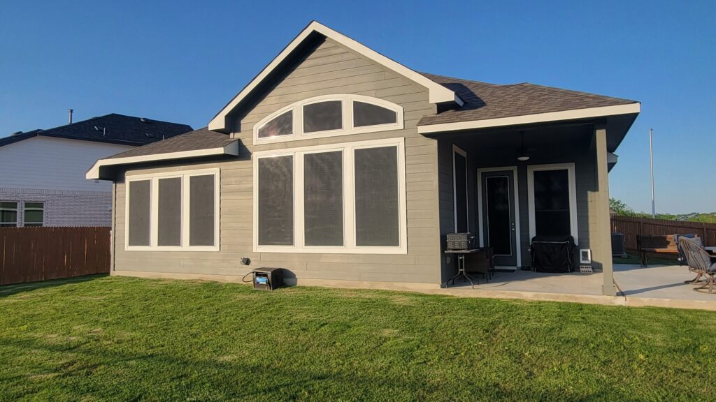 Professional solar screens installed on a modern gray Austin Texas home with large windows and covered patio